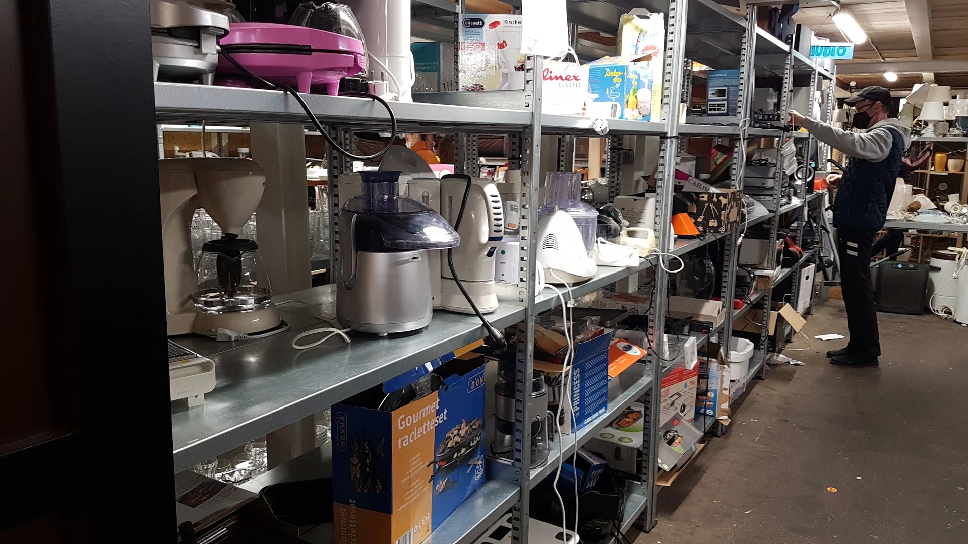Stellingen met huishoudelijke apparaten en keukengerei in een kringloopwinkel