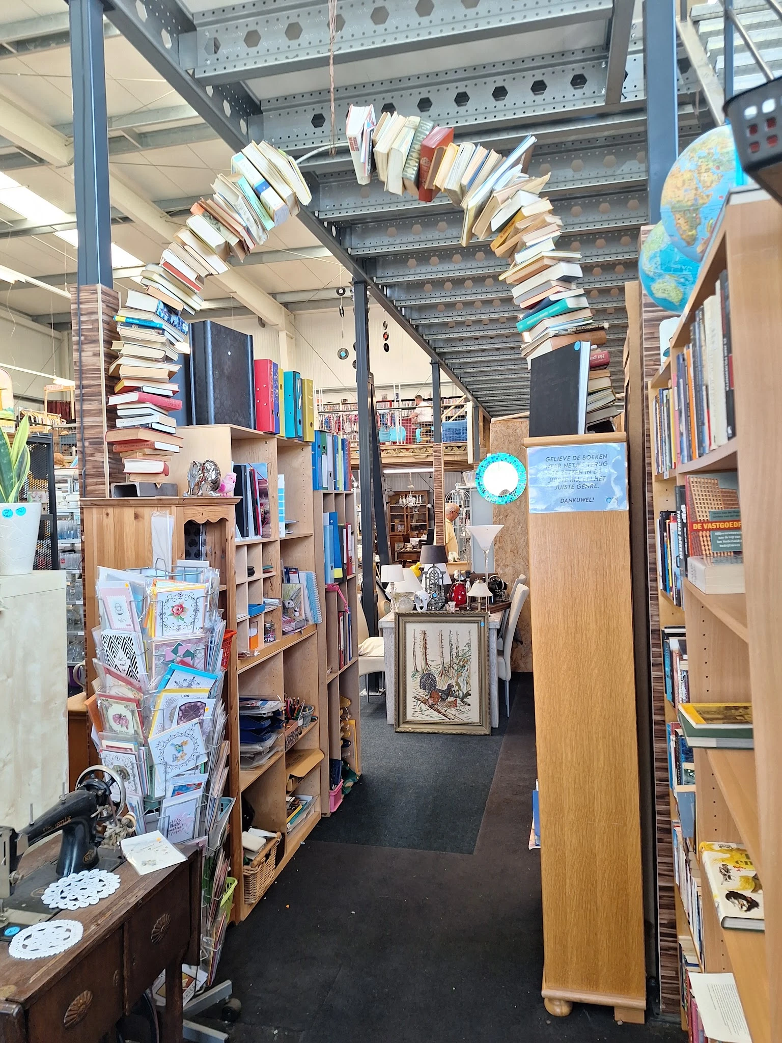 Overzicht van de winkelruimte met houten stellingen vol boeken, kasten en diverse tweedehandsartikelen