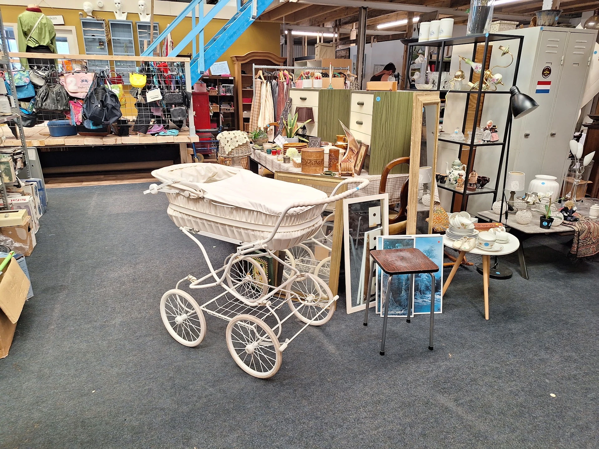 Winkelvloer van kringloopwinkel met vintage kinderwagen, meubels, kleding en huishoudartikelen uitgestald