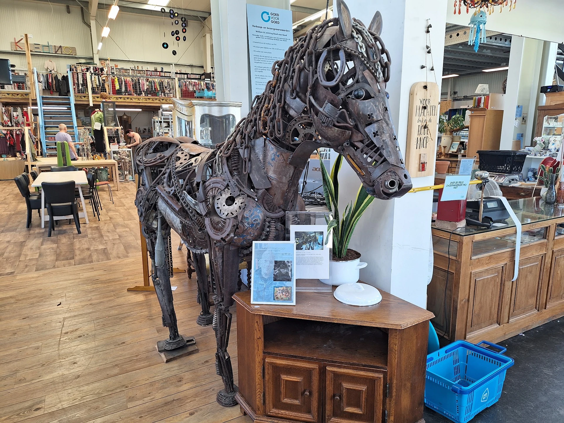 Zwart sculptuur van een paard gemaakt van gerecyclede materialen, tentoongesteld op een houten kast in de kringloopwinkel