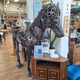 Zwart sculptuur van een paard gemaakt van gerecyclede materialen, tentoongesteld op een houten kast in de kringloopwinkel