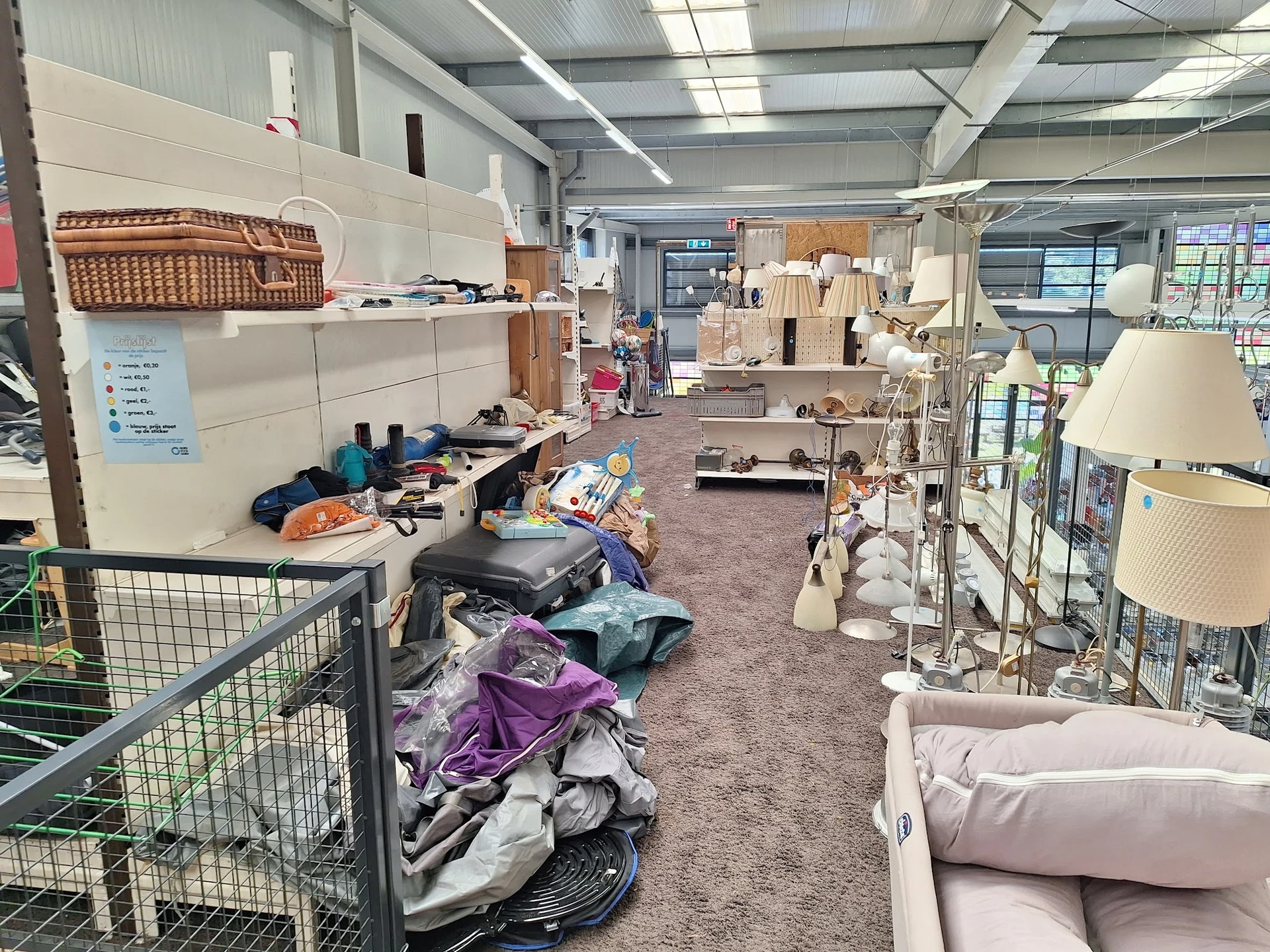 Winkelvloer met diverse tweedehandsartikelen, meubels en spullen verspreid over de grond en in rekken