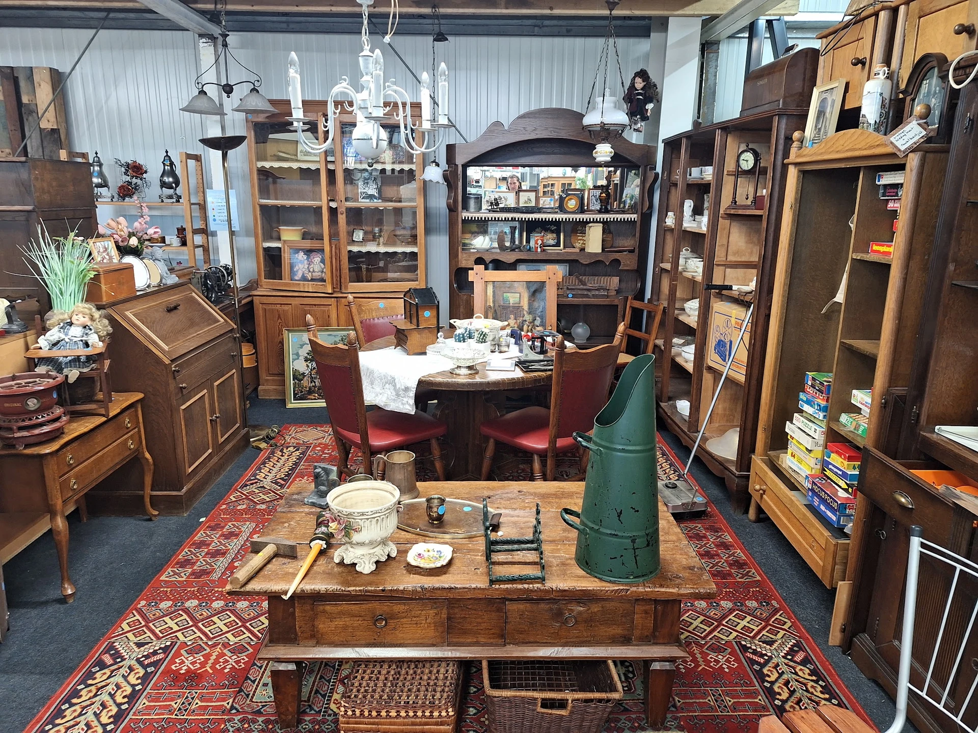 Overzicht van kringloopcentrum met houten meubels, kasten, tafel met servies, kroonluchter en rode tapijten