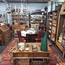 Overzicht van kringloopcentrum met houten meubels, kasten, tafel met servies, kroonluchter en rode tapijten