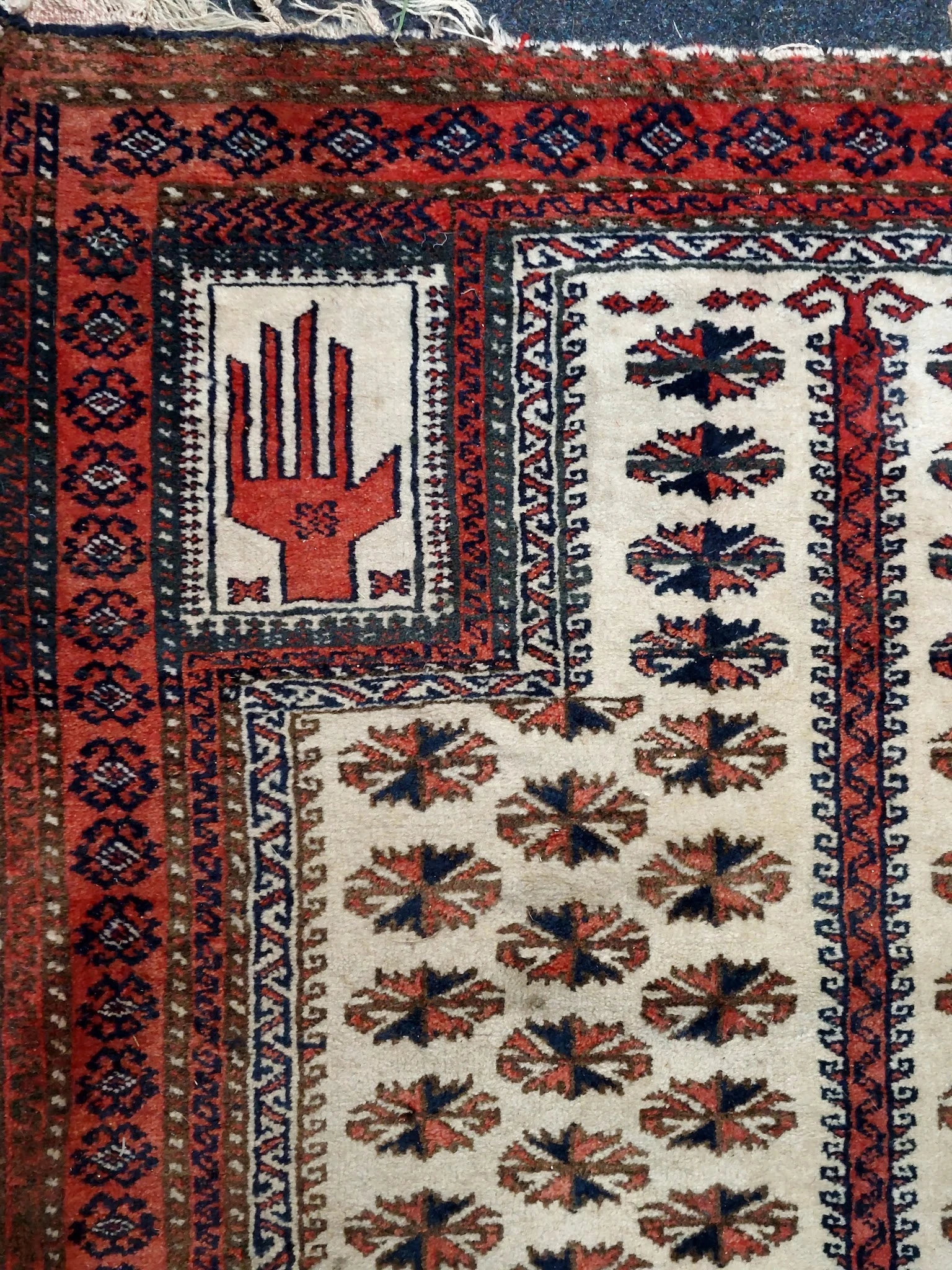 Close-up van een handgeweven tapijt met traditionele rode en zwarte handmotieven op cremekleurige achtergrond
