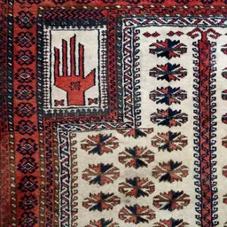 Close-up van een handgeweven tapijt met traditionele rode en zwarte handmotieven op cremekleurige achtergrond