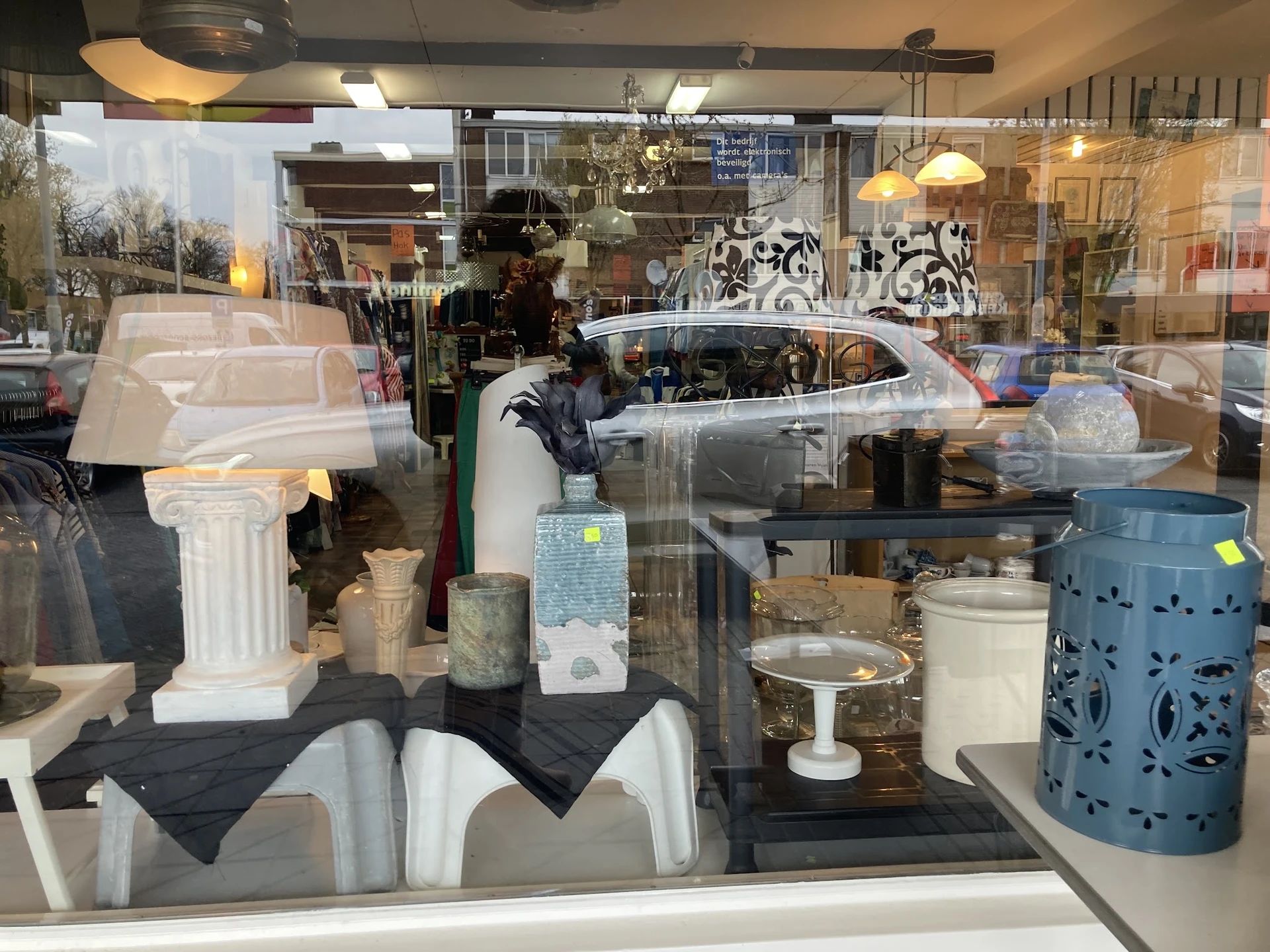 Etalage met diverse huishoudartikel, witte zuiltjes, blauwe metalen container en other home decor items