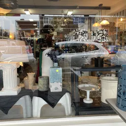 Etalage met diverse huishoudartikel, witte zuiltjes, blauwe metalen container en other home decor items