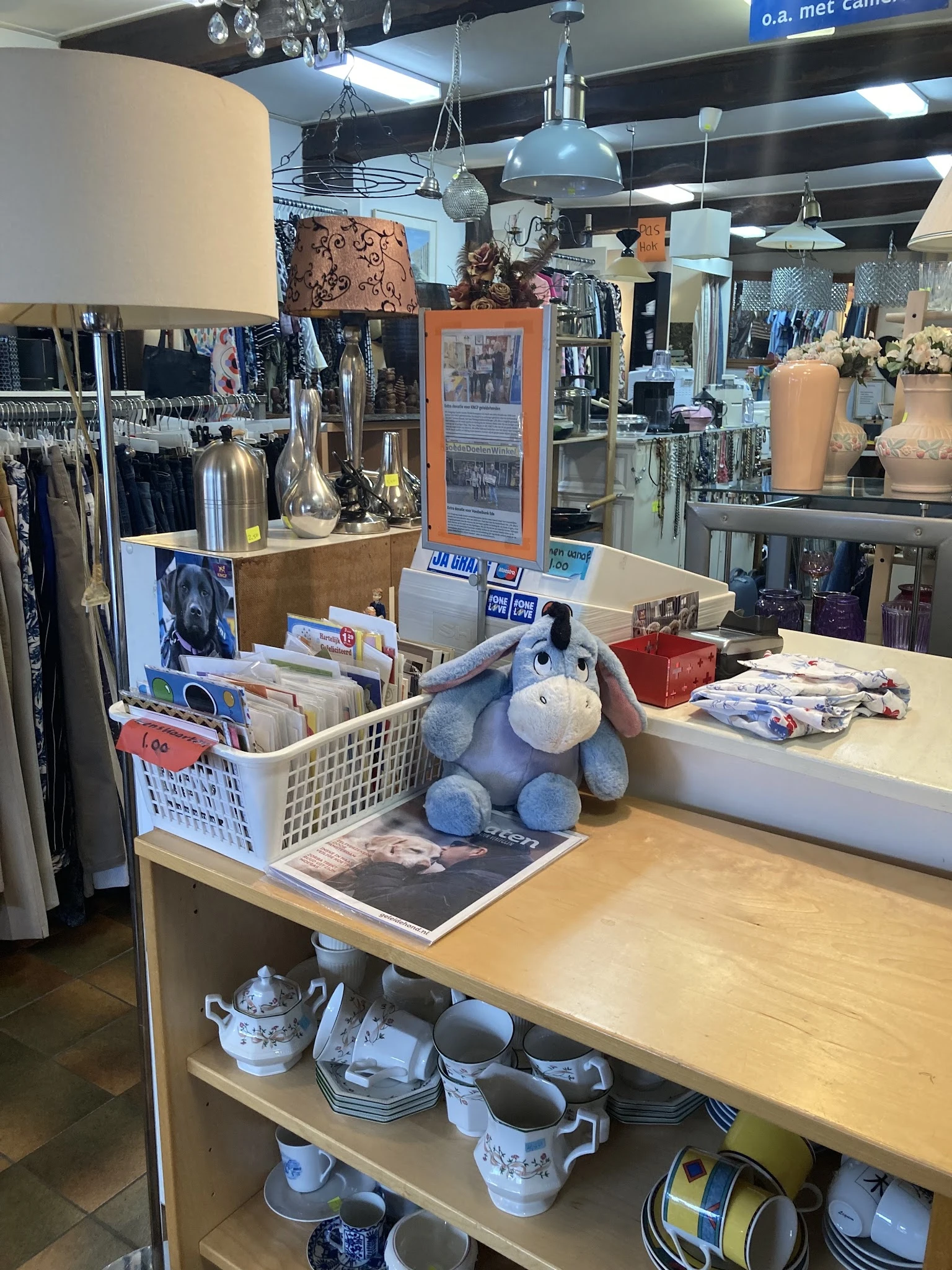 Toonbank met uitgestalde tweedehands artikelen: blauw knuffeldier, fotoboeken, vazen en overige decoratieve spullen in een kr