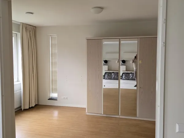 Lege winkelruimte met houten vloer, grote spiegelkast met witgoedapparatuur, raam met gordijnen en radiator