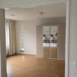 Lege winkelruimte met houten vloer, grote spiegelkast met witgoedapparatuur, raam met gordijnen en radiator