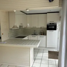 Witte keukenkasten met inbouwapparatuur, grijze tegels en donkergroene backsplash in een compacte keukenruimte