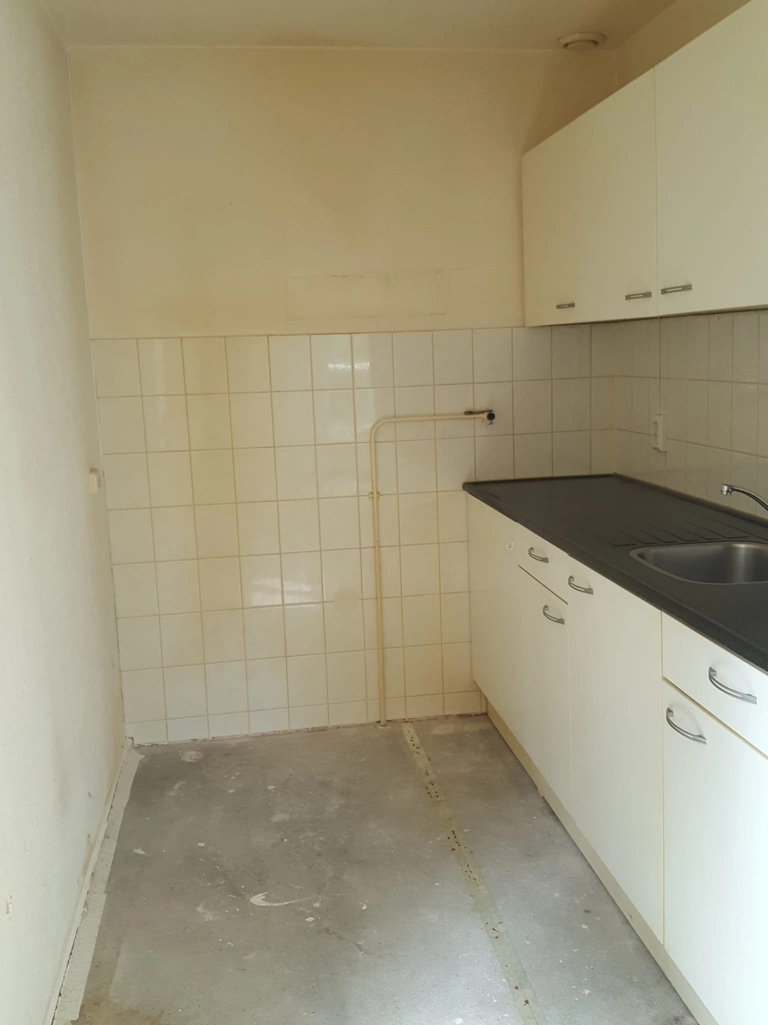 Lege keuken met witte kasten, zwart werkblad en tegelmuur in een ruimte zonder meubels