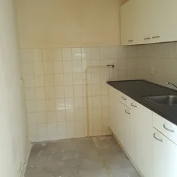 Lege keuken met witte kasten, zwart werkblad en tegelmuur in een ruimte zonder meubels