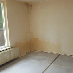 Lege kamer met witte muren, radiator en raam, mogelijk een winkelruimte in aanbouw of leegstand