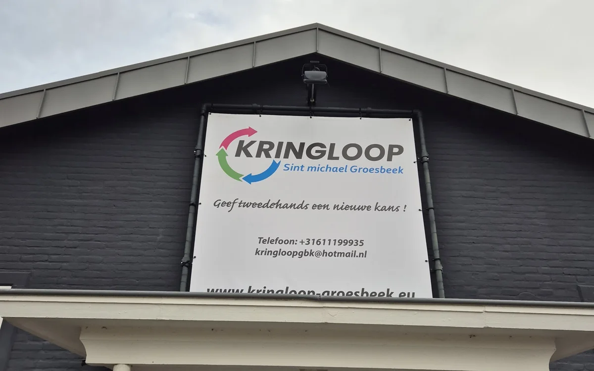 Donkergrijze gevel van kringloopwinkel met wit informatiebord, witte deur en raam eronder