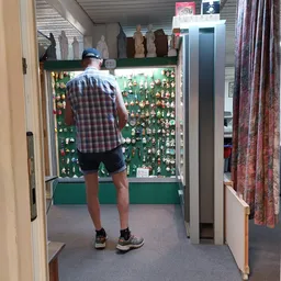 Man bekijkt vitrine met verzameling kleine speelgoedpopjes en verzamelobjecten op groene achtergrond