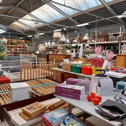 Winkelvloer met verschillende meubels, huishoudartikelen en decoraties; zichtbaar houten bedframe, laden, kaarsen, boeken en 