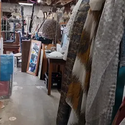 Smal gangpad tussen stellingen met diverse gebruikte spullen en meubels in een kringloopwinkel