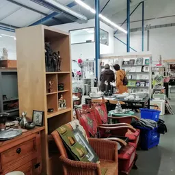 Ruime winkelruimte met diverse meubels, speelgoed en huishoudartikelen uitgestald, bezoekers in het achtergrond