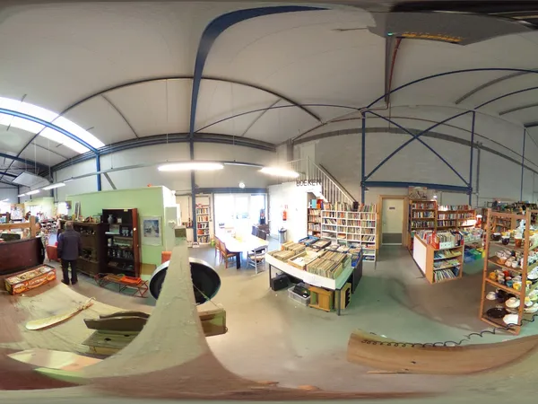 Winkelvloer met stellingen, boeken, spullen en verschillende afdelingen in een kringloopwinkel met grote raampartijen