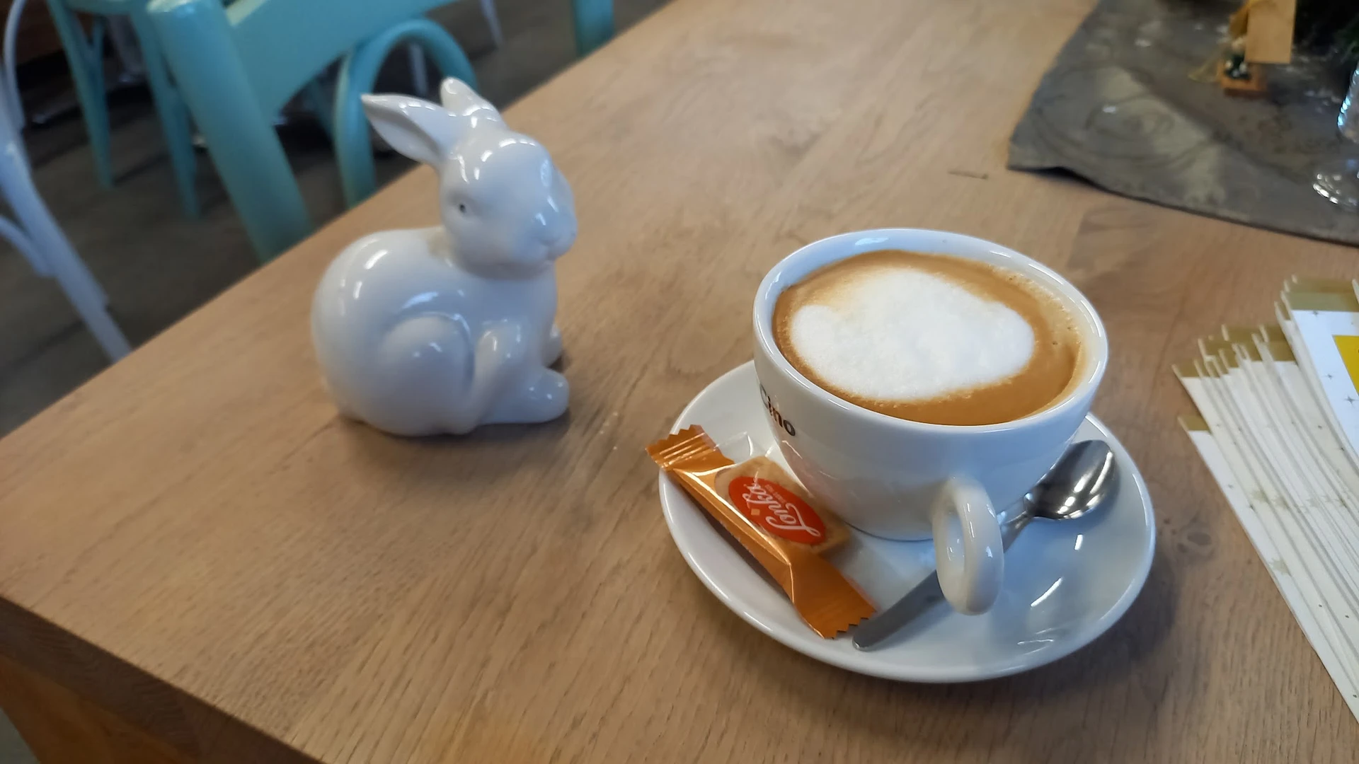 Kopje koffie met latte art op schoteltje met koekje, naast een wit konijntje decoratie