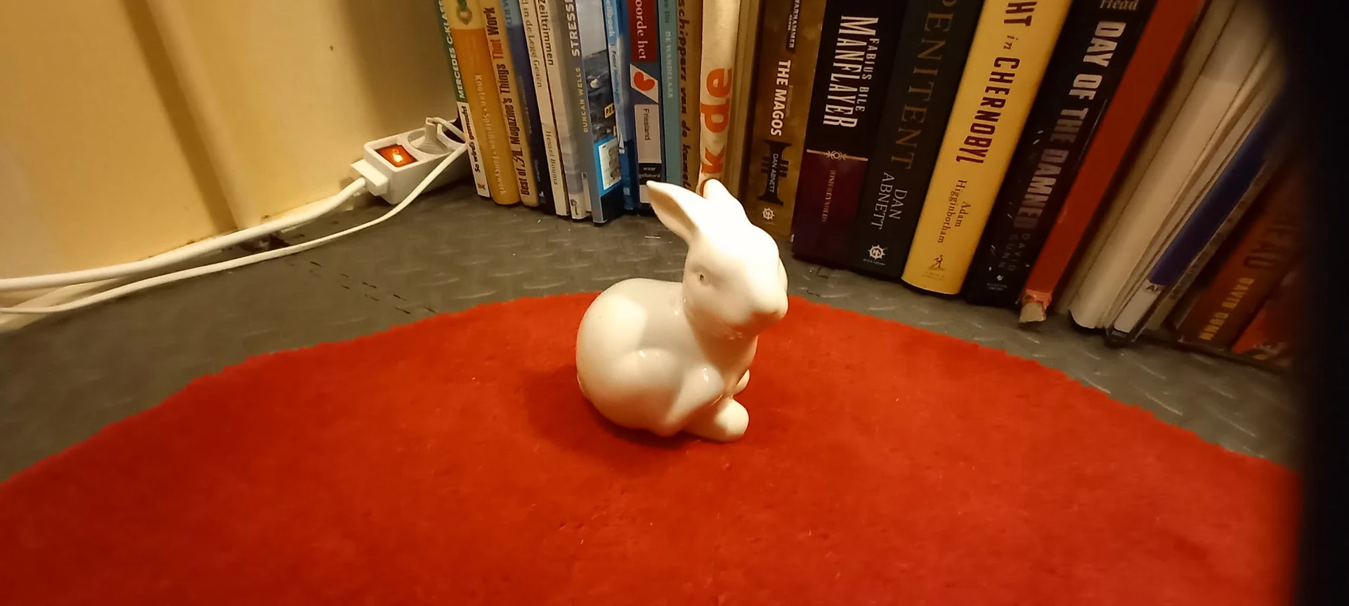 Wit keramiek konijnbeeldje op rood oppervlak voor boekenrekken