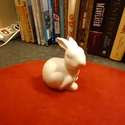 Wit keramiek konijnbeeldje op rood oppervlak voor boekenrekken