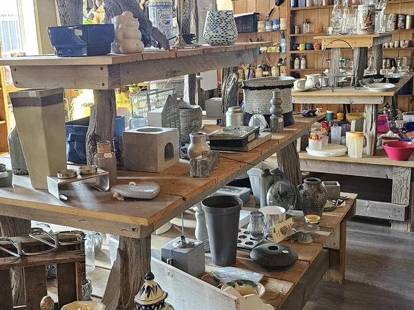 Overzicht van de kringloopwinkel met houten werktafels, stellingen vol huishoudelijke artikelen, decoratie en diversen