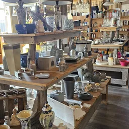 Overzicht van de kringloopwinkel met houten werktafels, stellingen vol huishoudelijke artikelen, decoratie en diversen