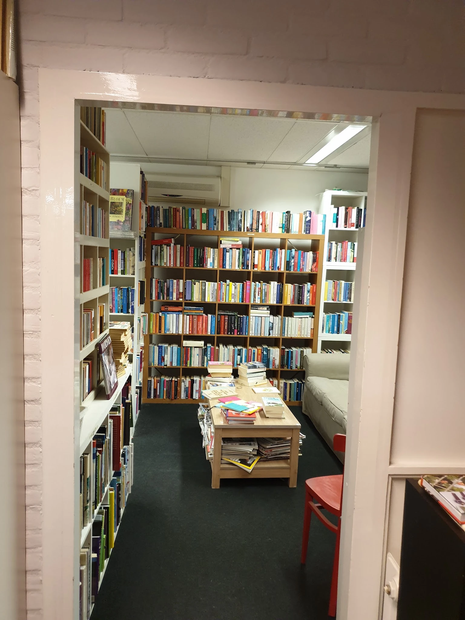 Boekenrekken langs de wanden van een smalle kringloopwinkelafdeling met een tafel met stapels boeken in het midden