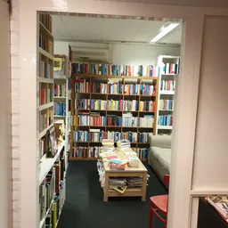 Boekenrekken langs de wanden van een smalle kringloopwinkelafdeling met een tafel met stapels boeken in het midden