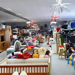 Binnenaanzicht van kringloopwinkel met meubels, kinderartikelen en diverse tweedehands spullen verspreid over de vloer en in 