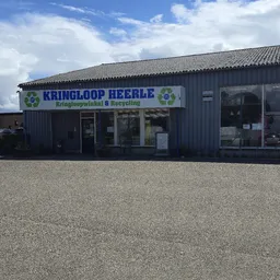Gevel van kringloopwinkel Heerle met blauwe letters en recycling logo's, zonnig weer