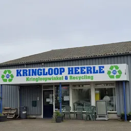 Gevel van kringloopwinkel Heerle met blauwe letters en groen recycle-logo's, stellage en ingang zichtbaar