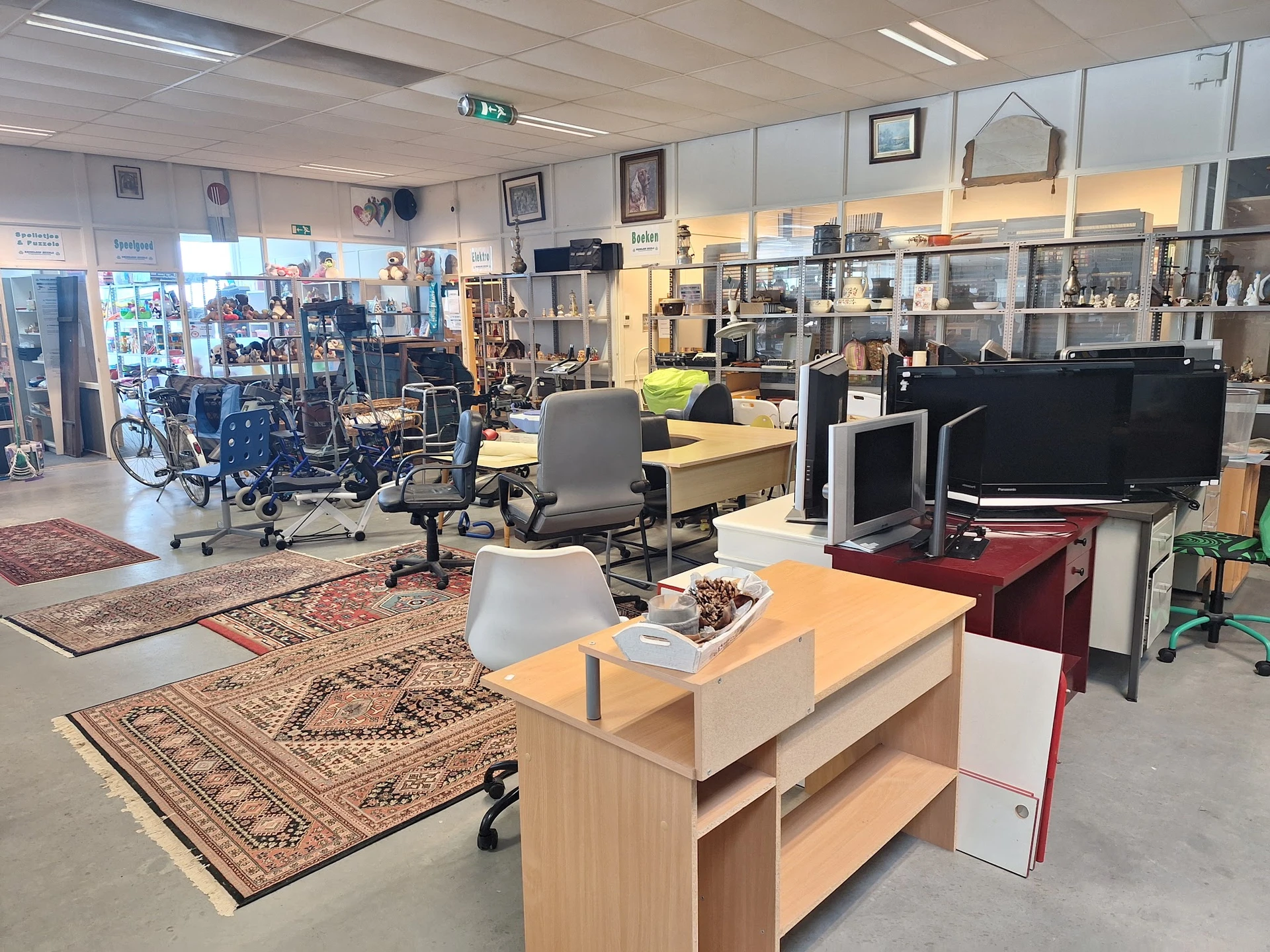 Winkelvloer met werktafels, stoelen, stellingen met spullen en diverse artikel in een kringloopwinkel