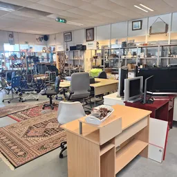 Winkelvloer met werktafels, stoelen, stellingen met spullen en diverse artikel in een kringloopwinkel