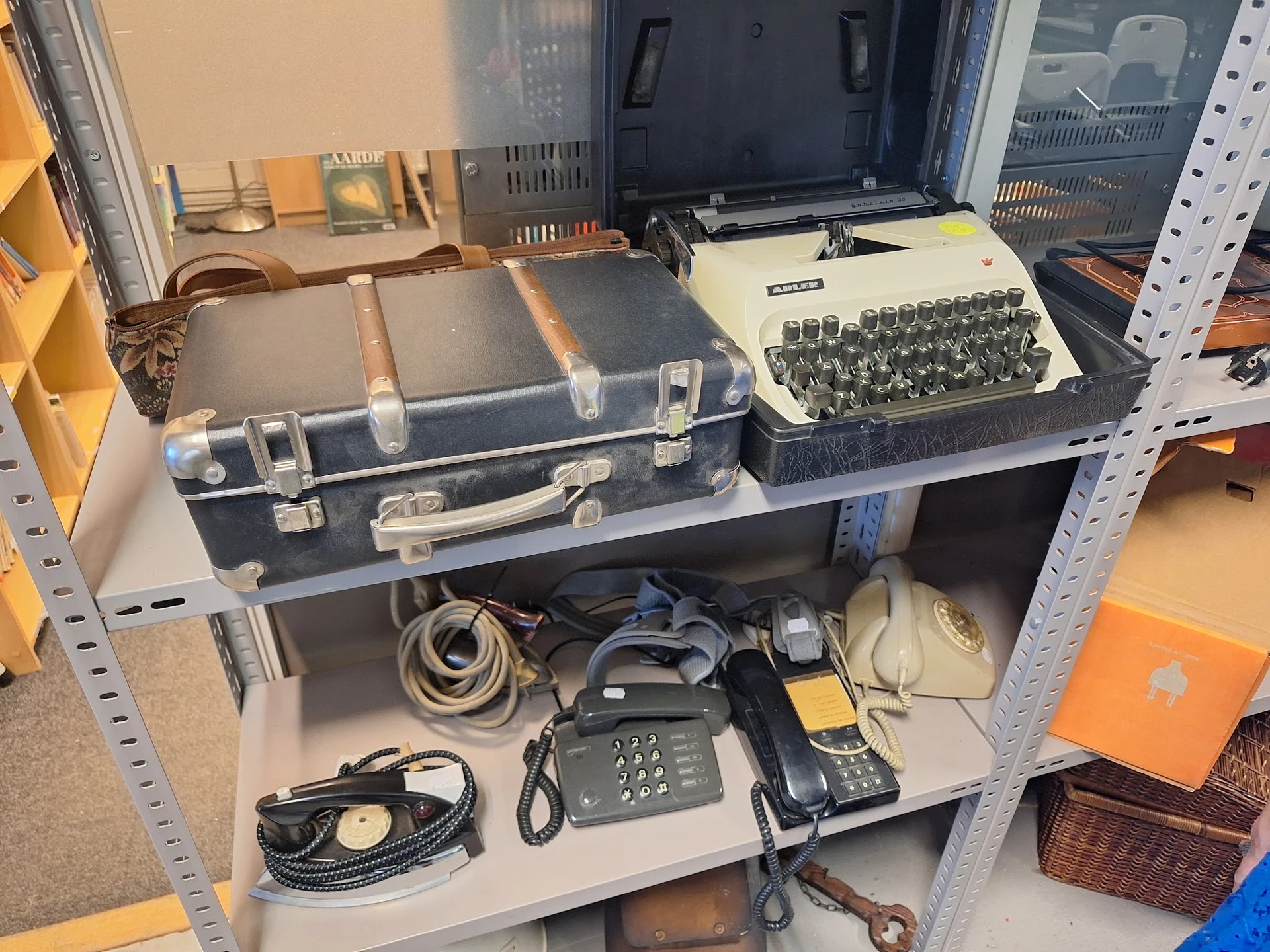 Stellingkast met vintage kantoorartikelen: schrijfmachine, oude telefoons, koffer en elektronica