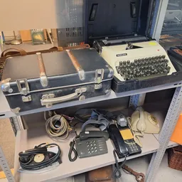 Stellingkast met vintage kantoorartikelen: schrijfmachine, oude telefoons, koffer en elektronica