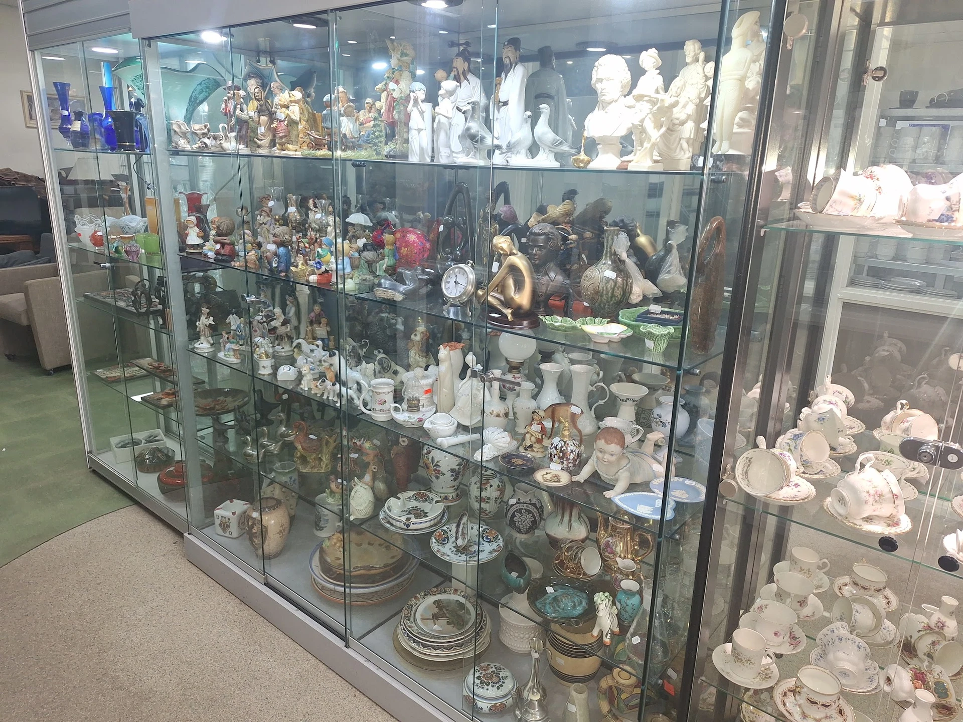 Glazen vitrinekast vol met verzamelde items zoals beeldjes, servies, decoratieve objecten en souvenirs.