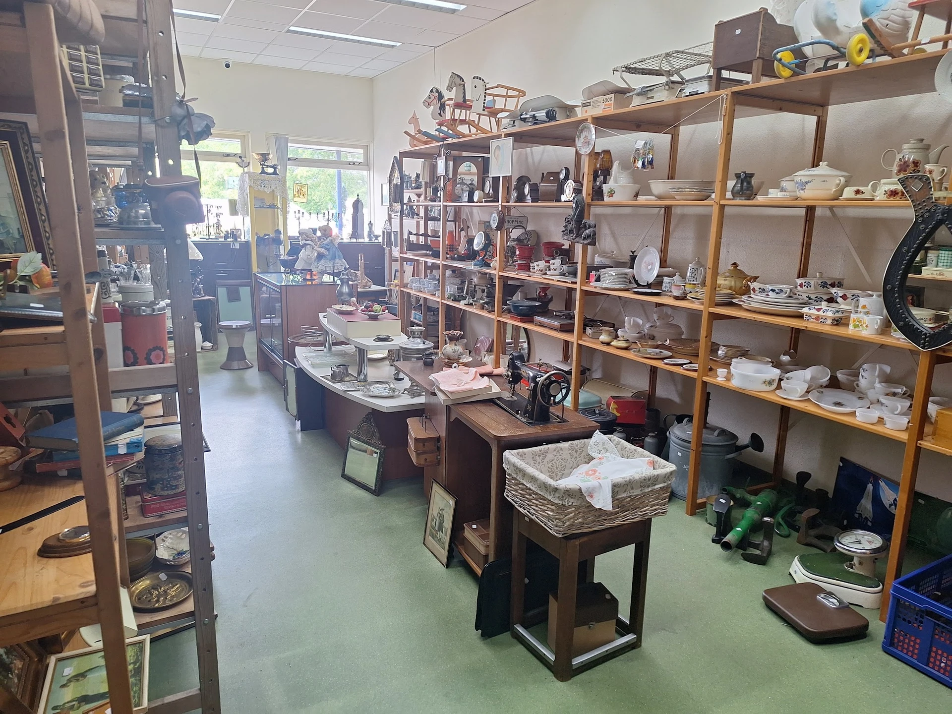 Winkelinterieur met houten stellingen vol serviesgoed, tafels met huishoudelijke spullen en groene vloer