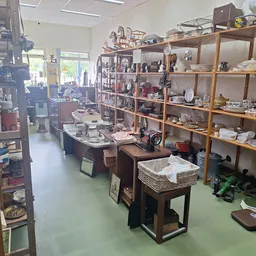 Winkelinterieur met houten stellingen vol serviesgoed, tafels met huishoudelijke spullen en groene vloer