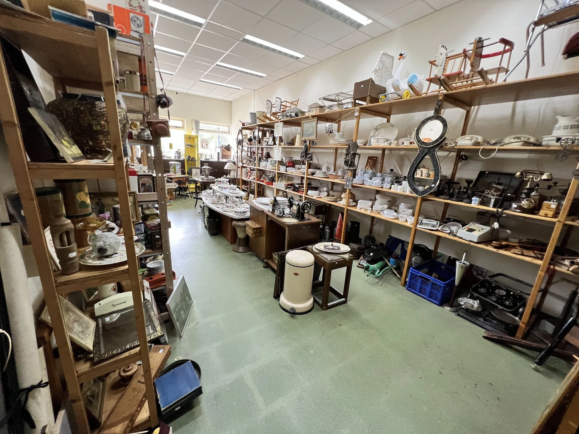 Overzicht van de winkelvloer met houten stellingen volgeladen met huishoudartikelen, servies en diversen