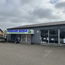 Gevel van kringloopwinkel Heerle met blauwe naam en groene logo's, metalen constructie met grote ramen