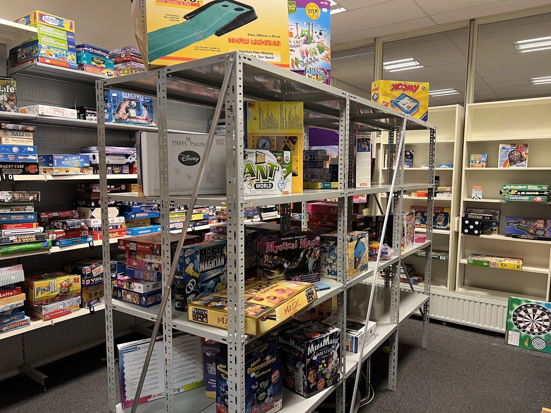 Stellingen met tweedehands speelgoed, bordspellen en dvd's in een kringloopwinkel