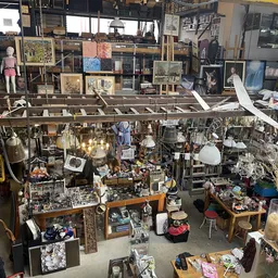 Overzicht van kringloopwinkel met diverse tweedehands goederen: lampen, kunstwerk, meubels, servies en decoratieartikelen op 