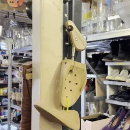 Beige schoenrekje met gaten tegen een muur, opgehangen aan een houten haak
