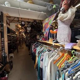 Overzicht van het interieur van een kringloopwinkel met kledingrekken, potten en pannen, en verschillende spullen uitgestald