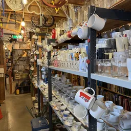 Stellingen vol huishoudelijke artikelen en serviesgoed in een kringloopwinkel