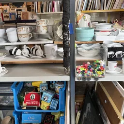 Schappen met huishoudelijk servies, kopjes, borden en decoratieve items in een kringloopwinkel